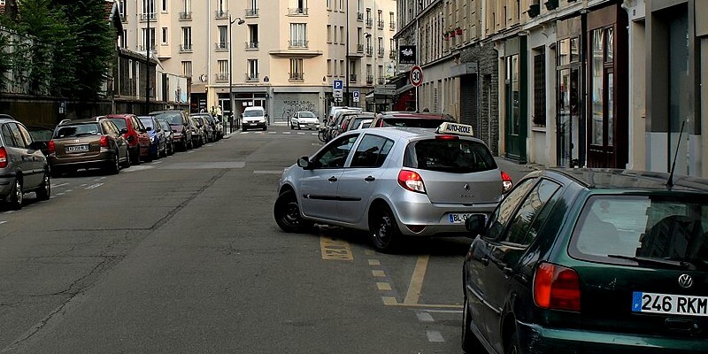 Voitures stationnées dans une rue avec une voiture qui veut faire un créneau