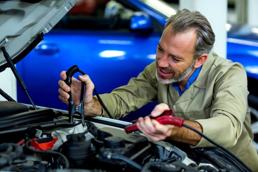 Mécanicien recharge une batterie de voiture à l'aide de pinces