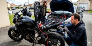 Couple qui essaie de recharger la batterie d'une moto avec celle d'une voiture